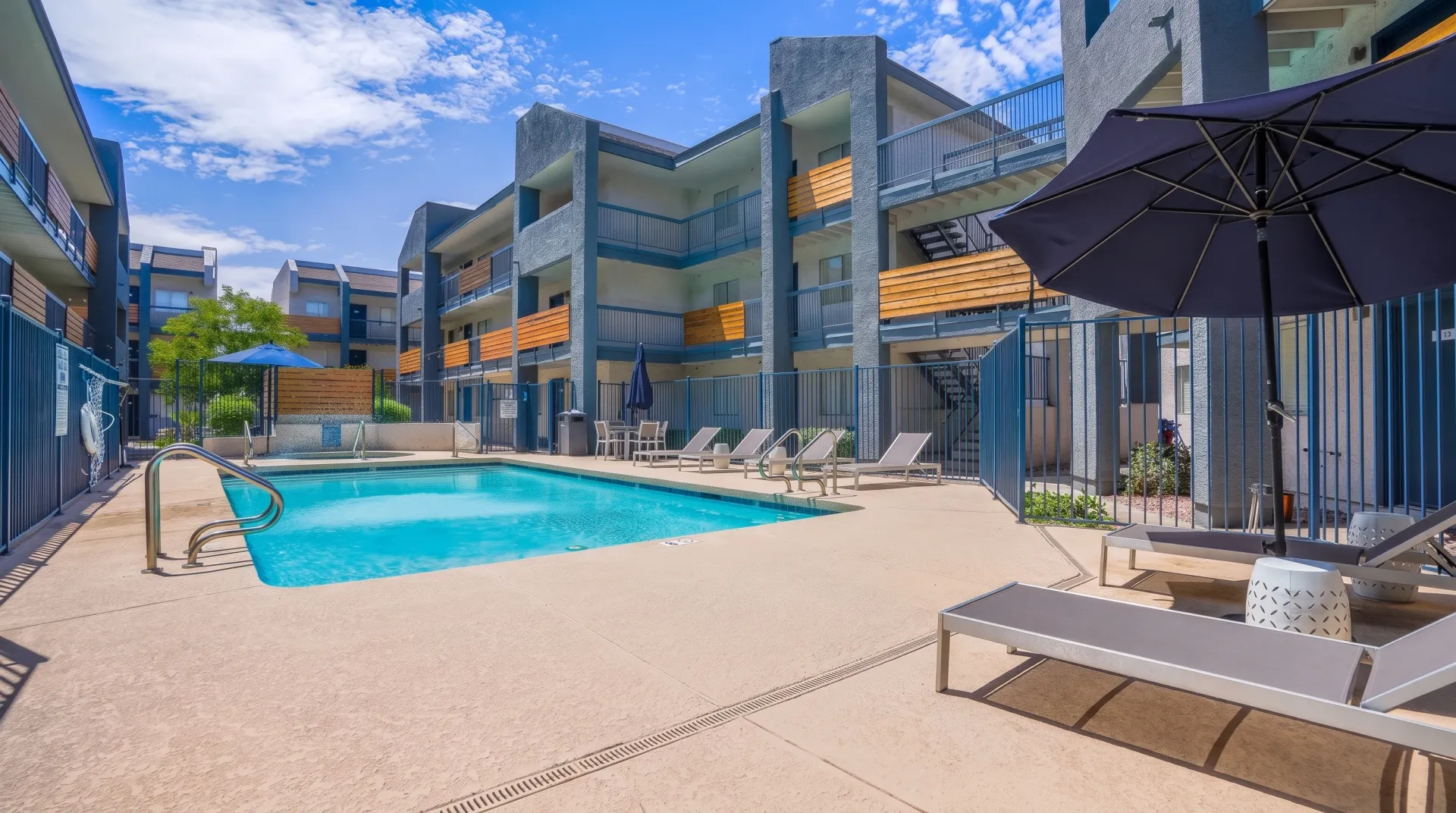 Pool with lounge chairs, umbrellas, modern apartment buildings, clear blue sky