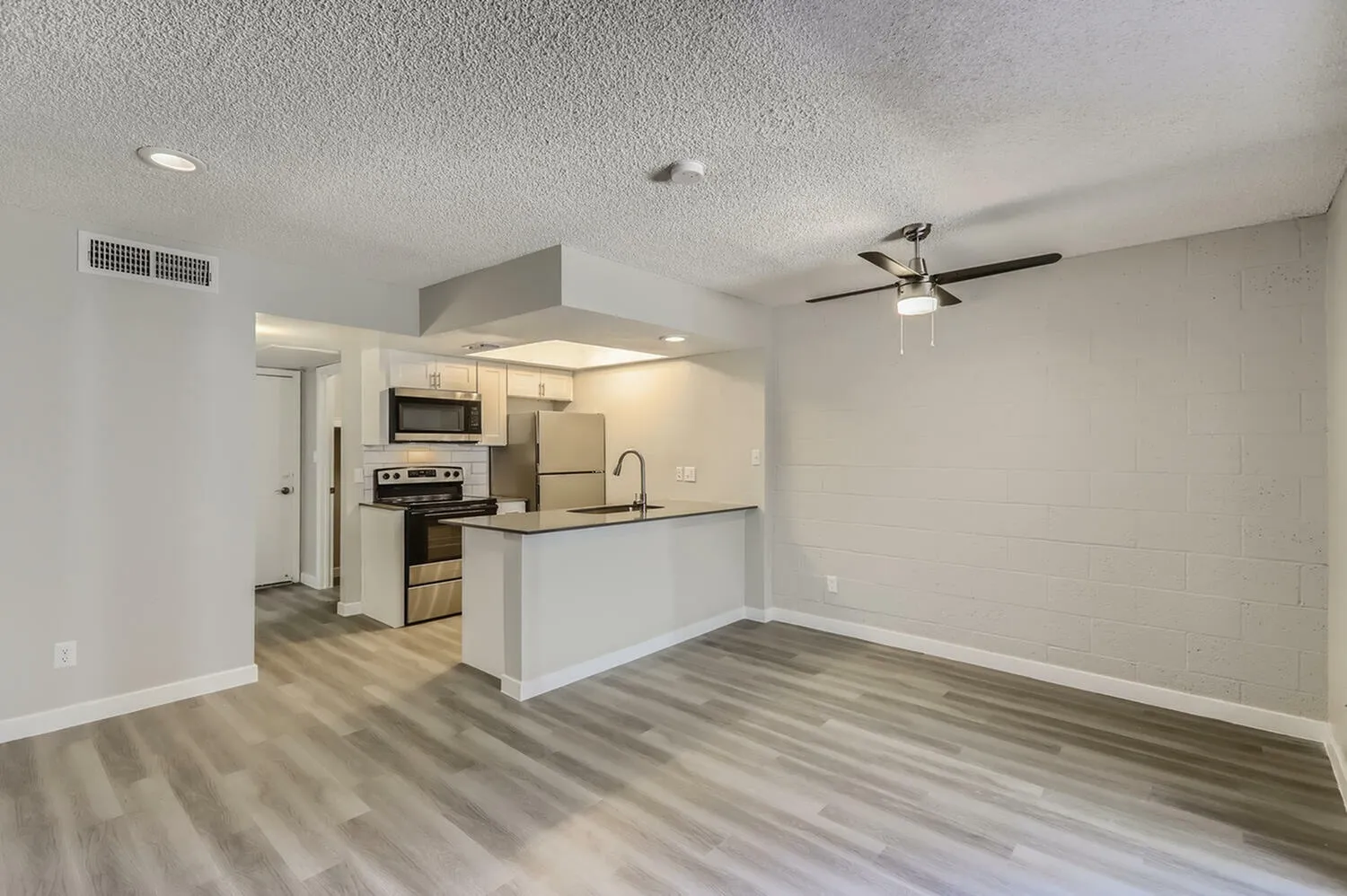 Kitchen and living room, wood-style plank flooring, white cabinetry, stainless appliances, ceiling fan