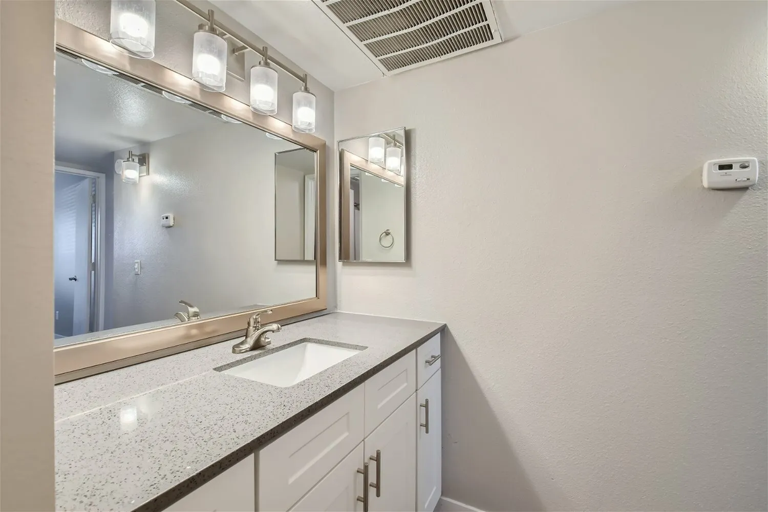 Bathroom vanity, white cabinetry, quartz countertops, framed mirror, vanity lighting
