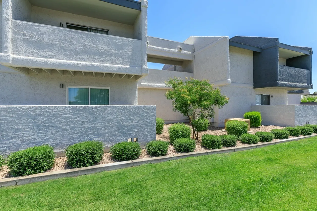 Modern residential building with concrete and stone facade, manicured landscaping, green lawn, architectural balconies