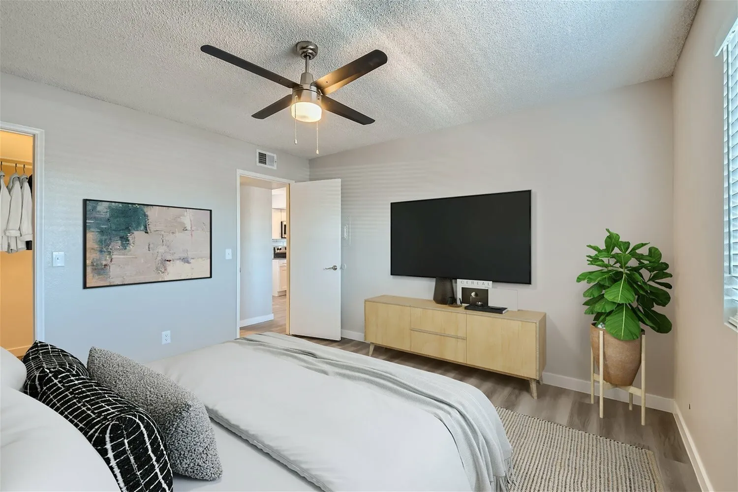 Primary bedroom, TV mounted on wall, wood-style plank flooring, ceiling fan with light