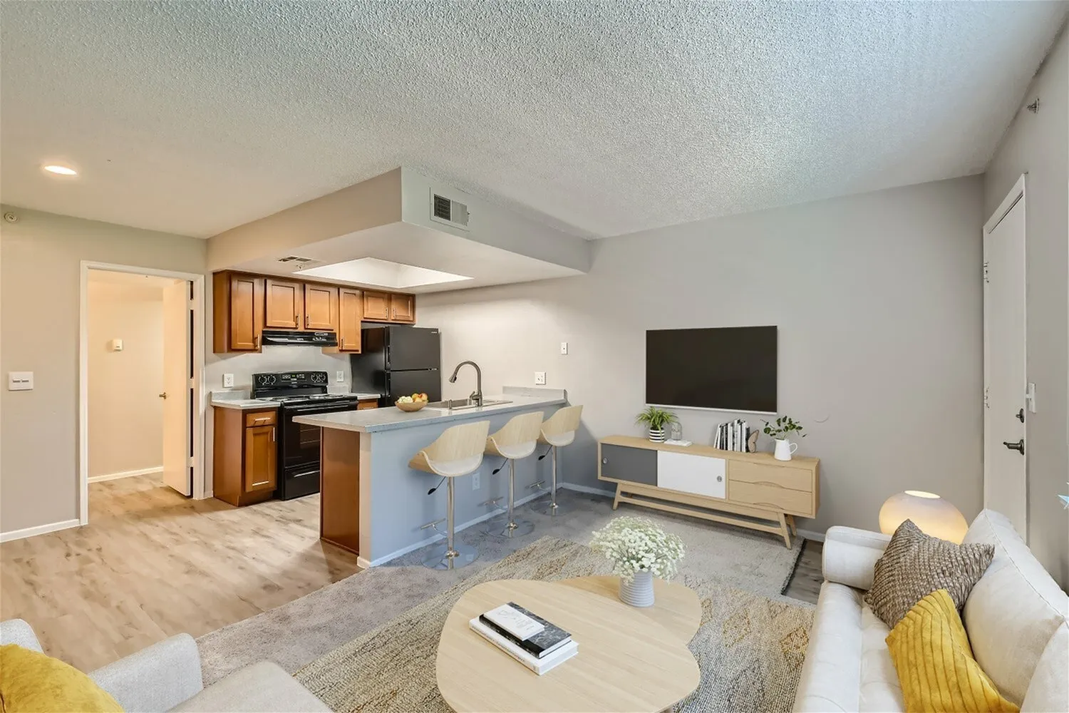 Open concept living room and kitchen with wood-style plank flooring, wood cabinetry, stainless appliances, island seating, television, and neutral décor