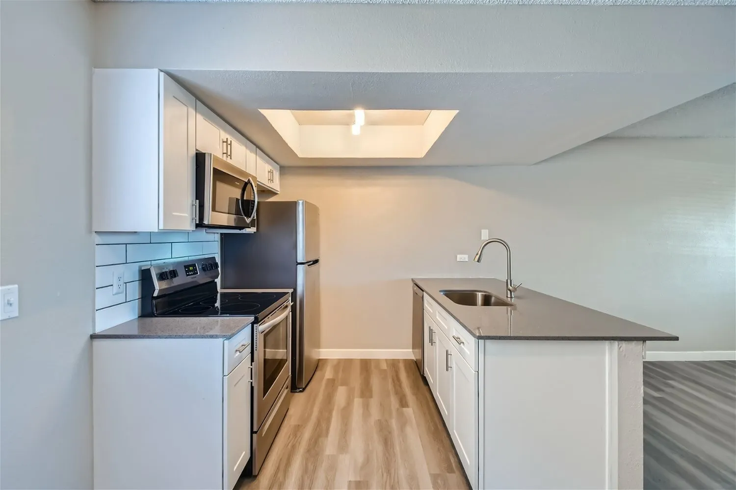 Kitchen, white shaker cabinetry, stainless appliances, gray countertops, wood-style plank flooring