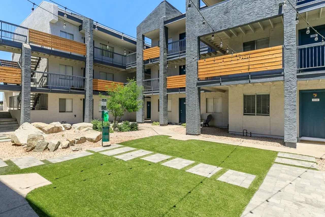 Courtyard with green lawn, stepping stone pathway, decorative boulders, concrete planter, multi-story residential buildings with wood siding and stone exterior accents