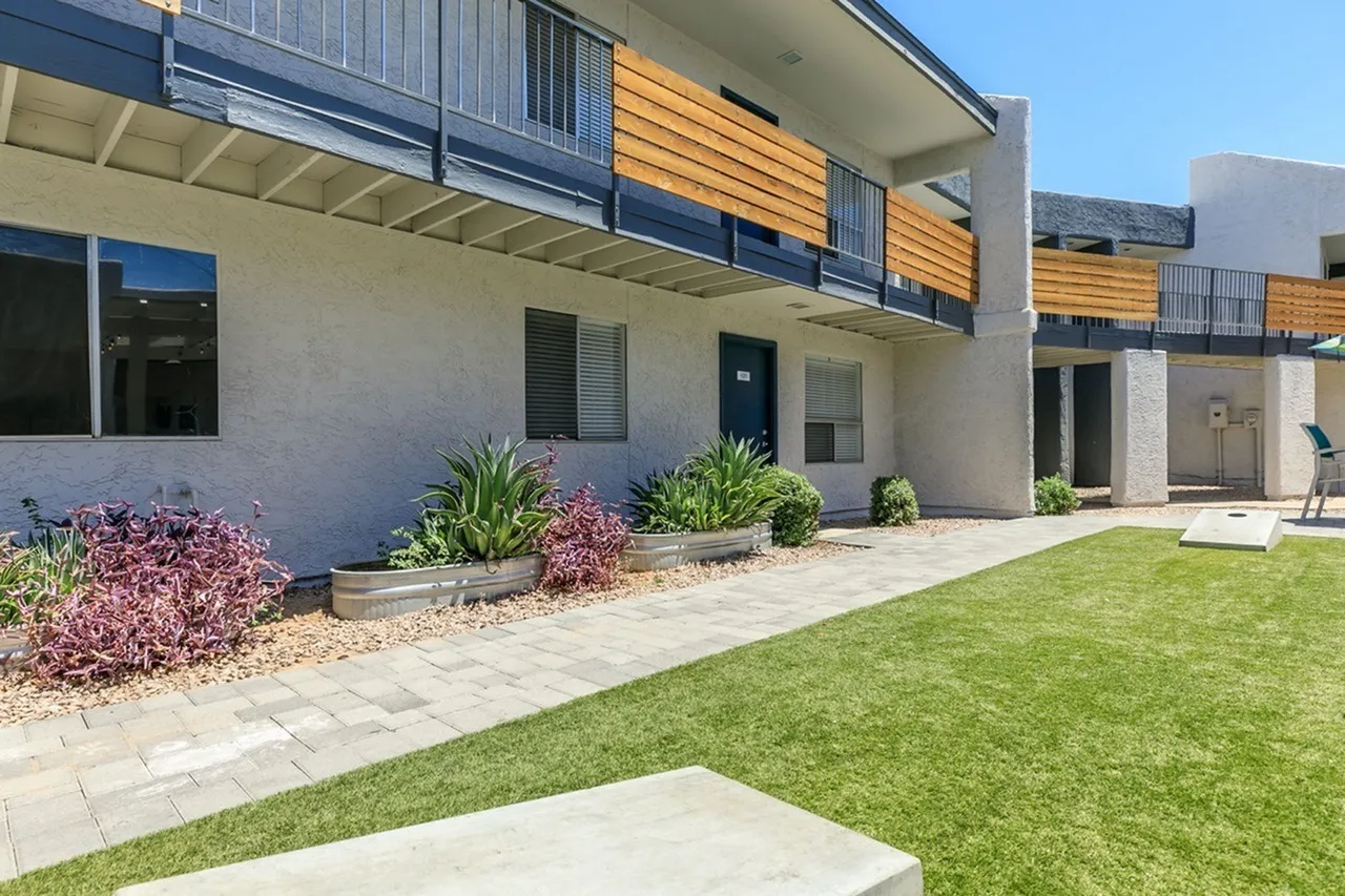 Building exterior with patio, manicured lawn, planter beds with shrubs, wooden balcony accents