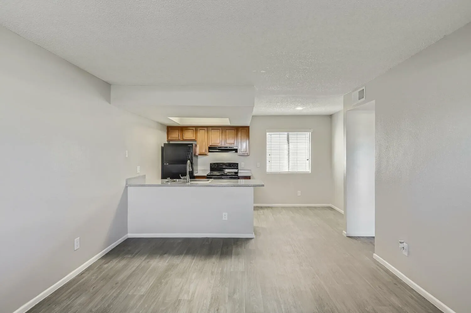 Kitchen and living space, wood-style plank flooring, wood cabinetry, stainless appliances, island counter