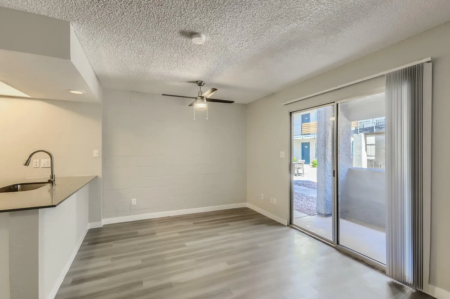 Living room, wood-style plank flooring, ceiling fan, sliding glass patio doors, white walls