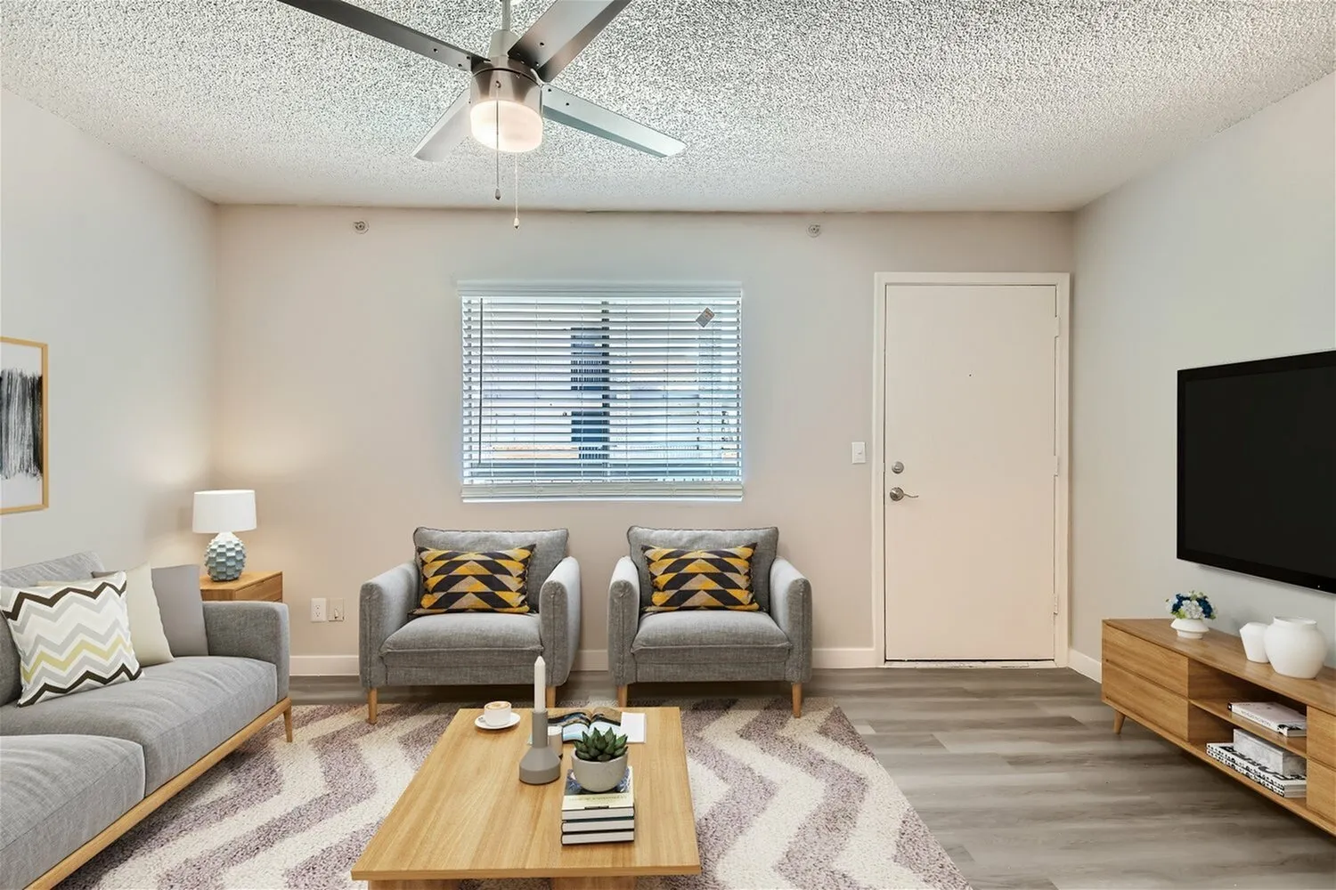 Living room with wood-style plank flooring, ceiling fan, gray seating, patterned rug, wood coffee table