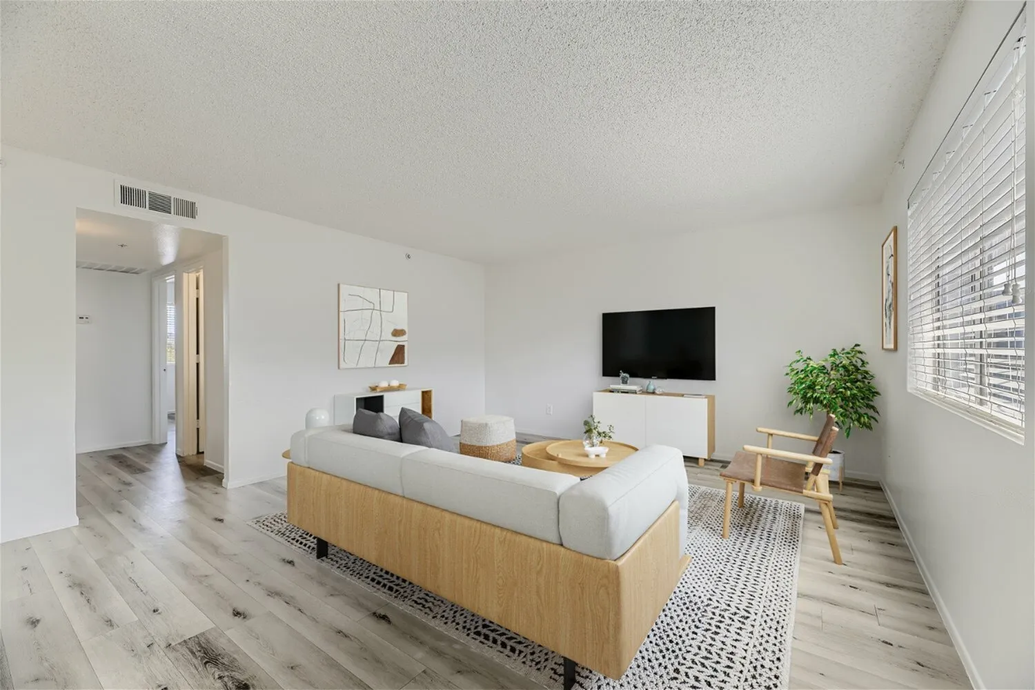Living room, wood-style plank flooring, light oak media console, gray upholstered sofa, potted plants