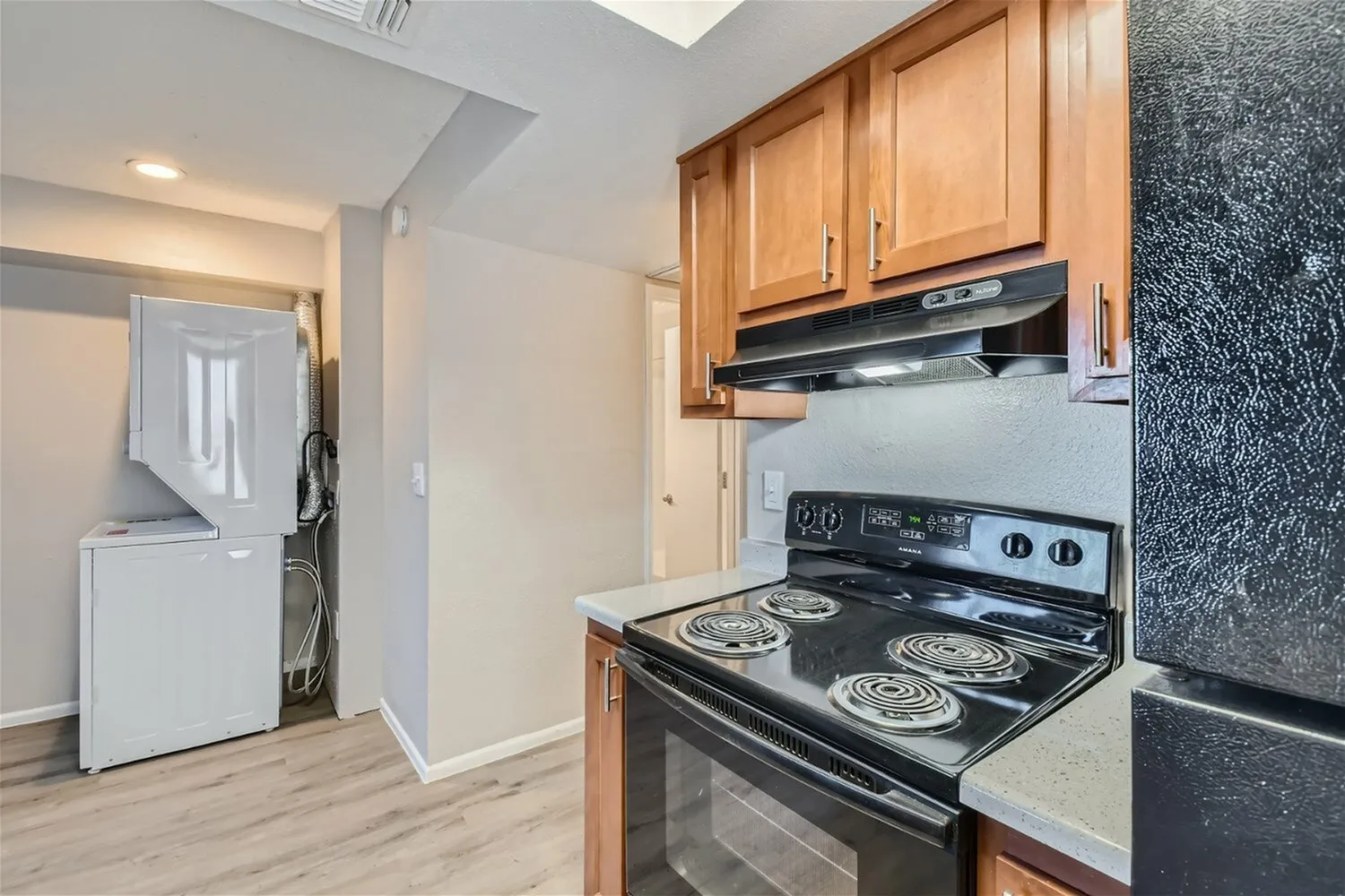 Kitchen, wood cabinetry, black electric range, wood-style plank flooring, range hood