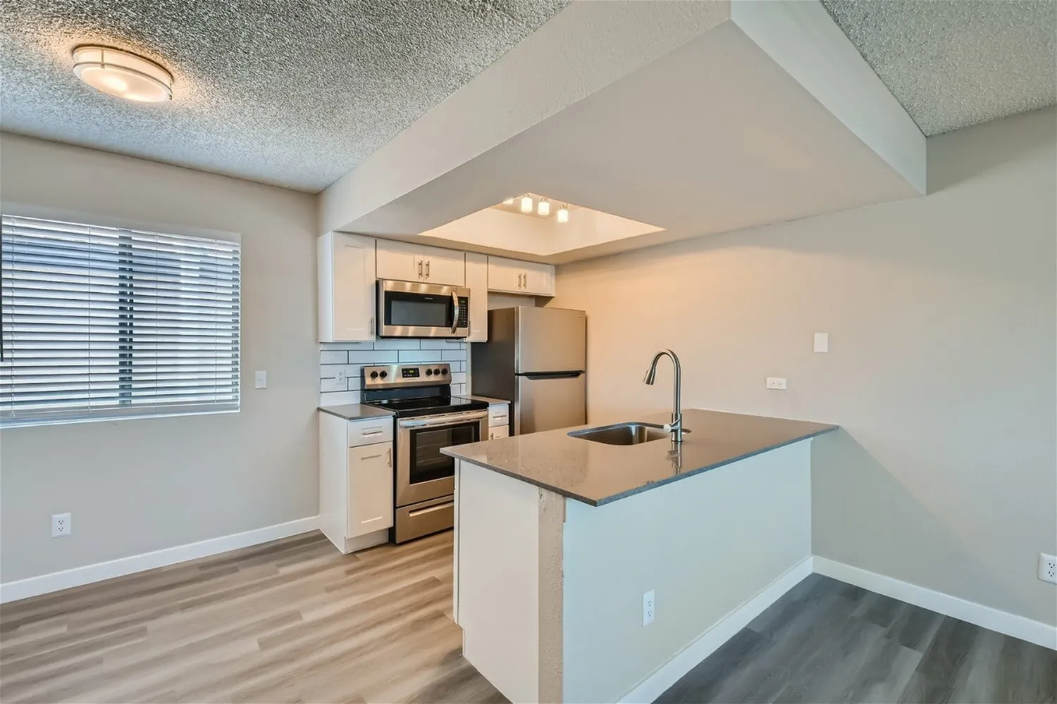 Kitchen, white cabinetry, stainless steel appliances, wood-style plank flooring, island with sink