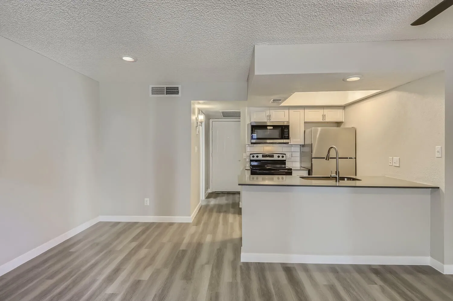 Open concept living room and kitchen, wood-style plank flooring, stainless appliances, gray countertops
