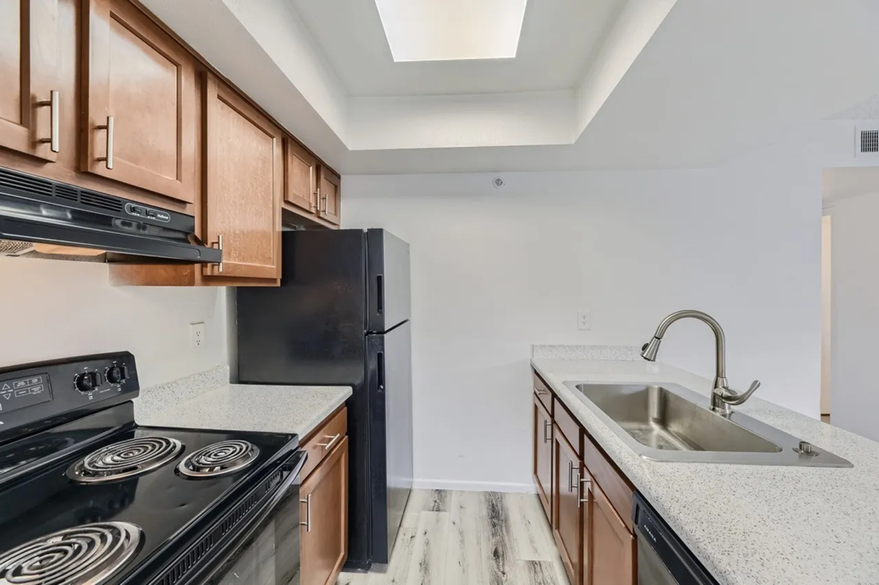 Kitchen, wood cabinetry, black electric range, black refrigerator, quartz countertops, stainless sink, wood-style plank flooring