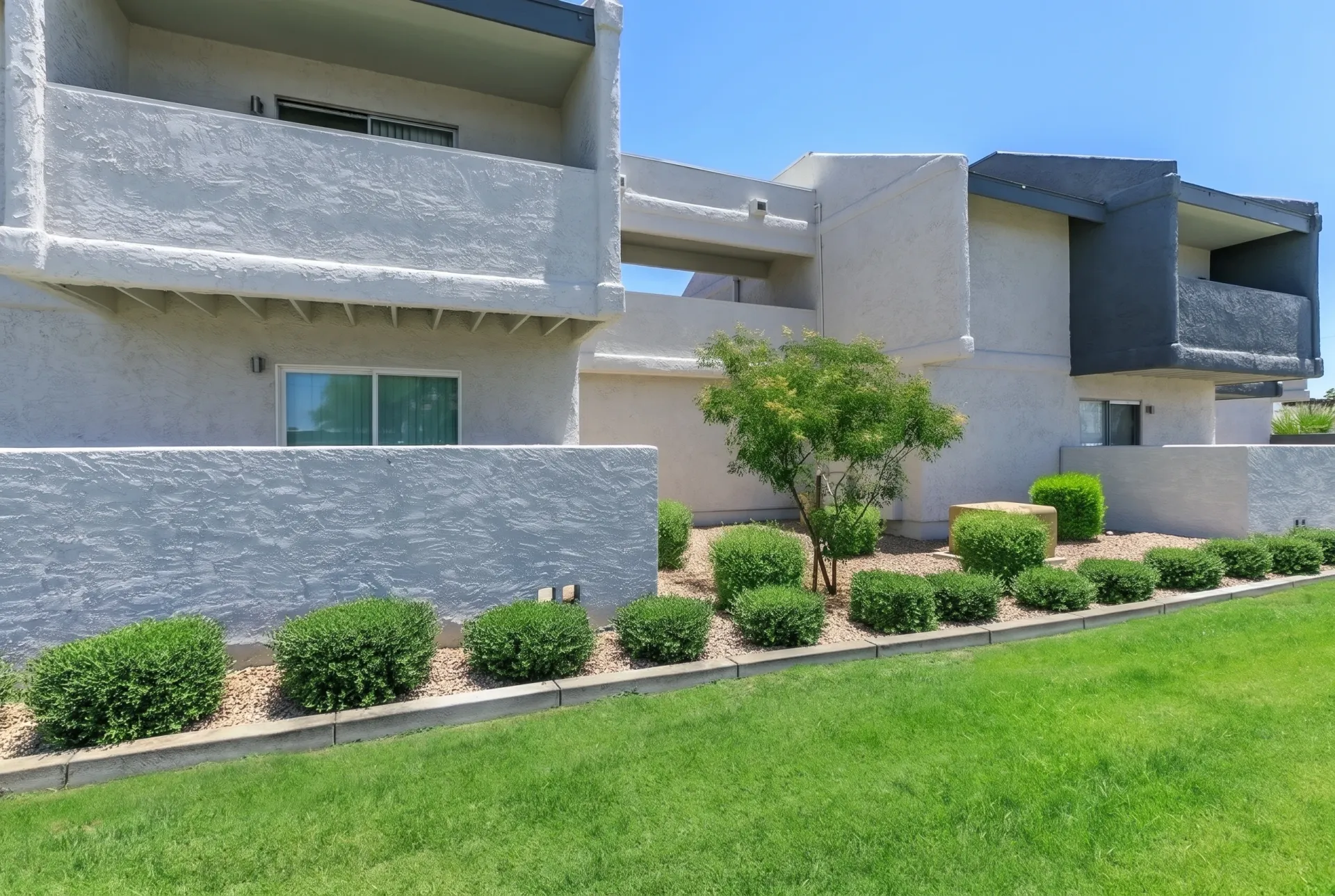 Modern residential building with concrete and stone facade, manicured landscaping, green lawn, architectural balconies