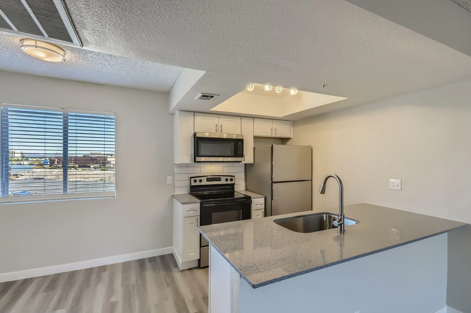 Kitchen with white shaker cabinetry, quartz countertops, stainless appliances, island counter, wood-style plank flooring, windows with blue shutters