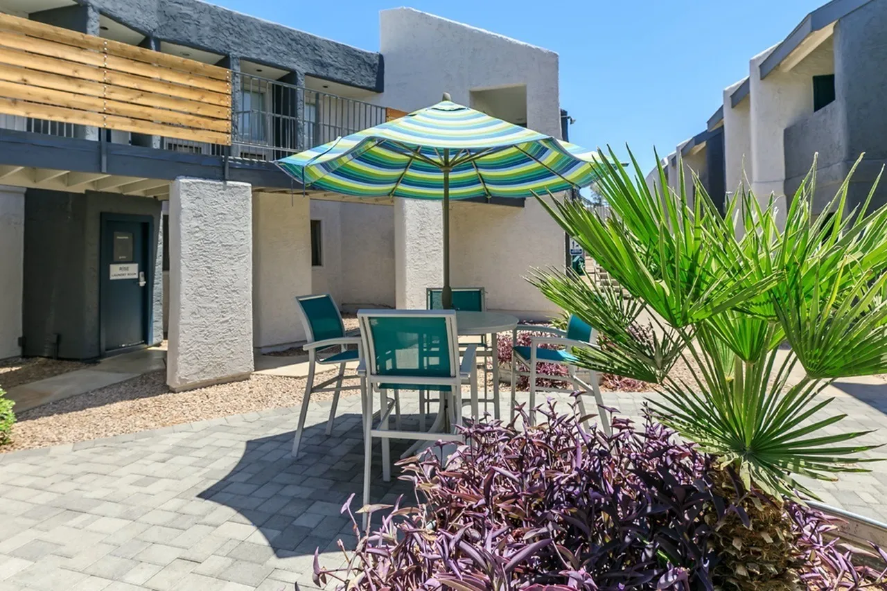 Outdoor courtyard, striped green and white umbrella, teal lounge chairs, tropical plants