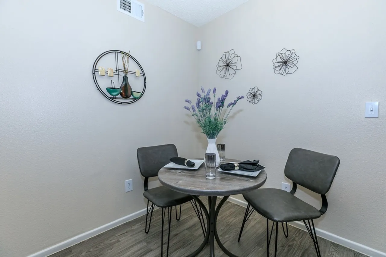 Dining area, round marble-style table, dark upholstered chairs, wall art, decorative floral arrangement, wood-style plank flooring
