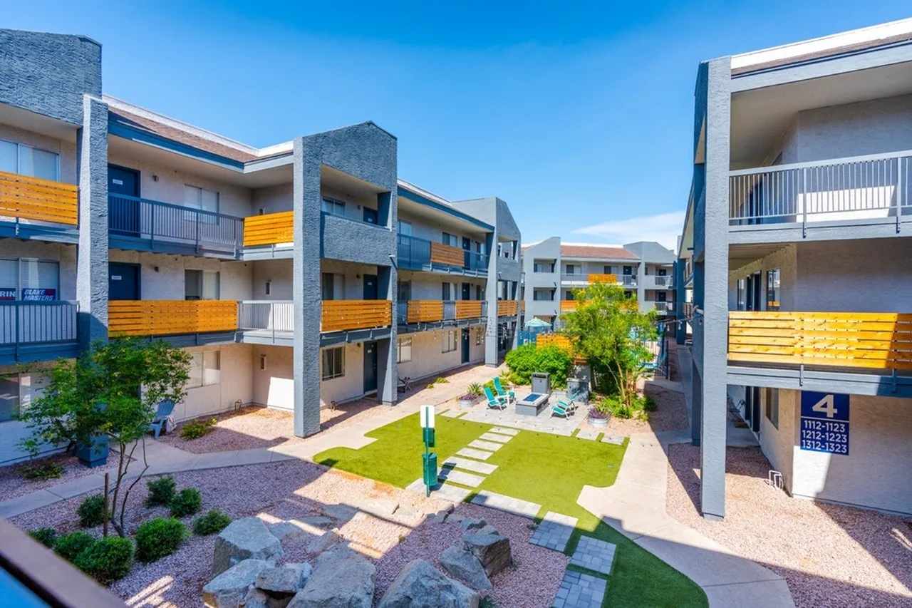 Courtyard with green lawn, stone pathways, multi-story residential buildings, yellow balcony accents