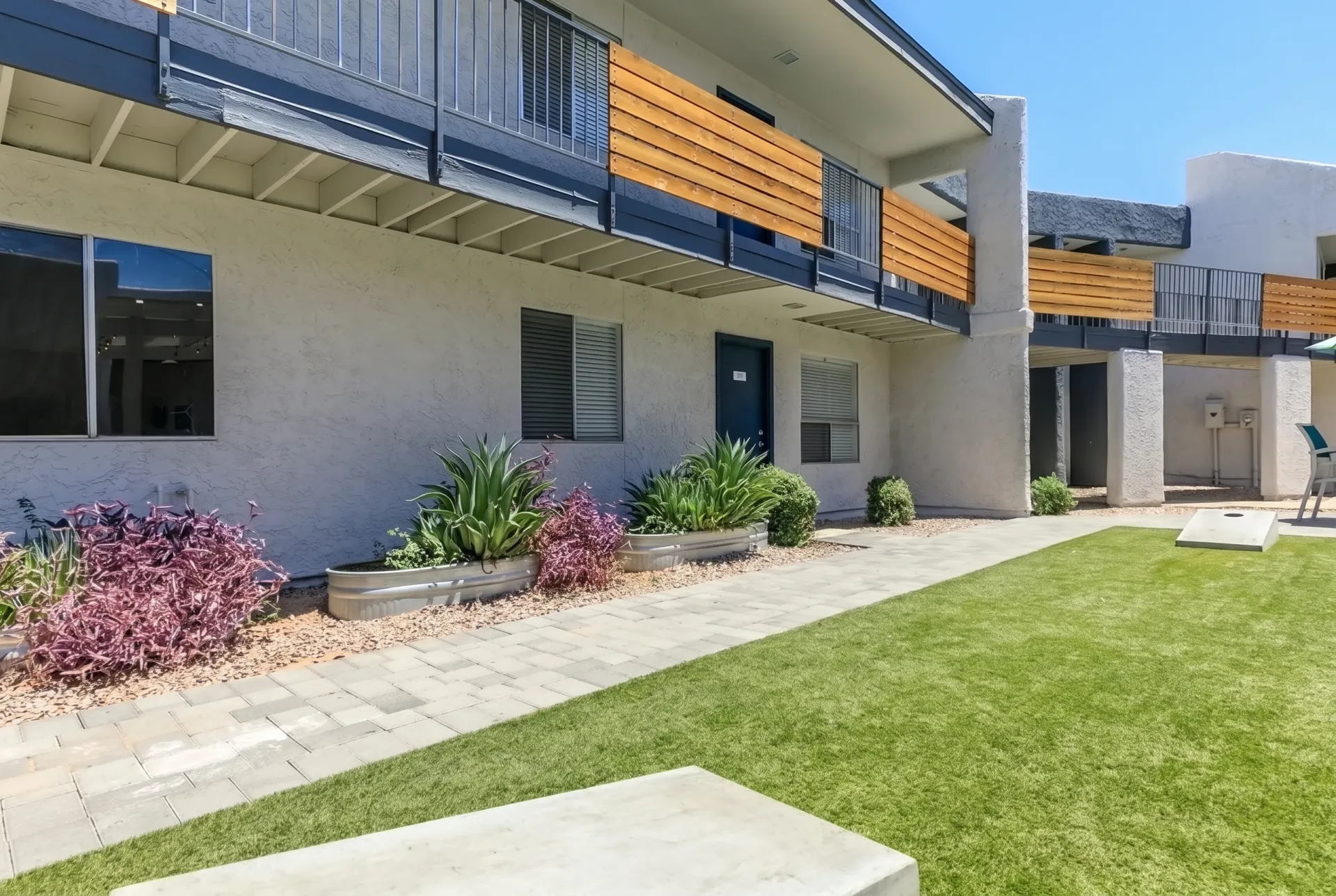 Building exterior with patio, manicured lawn, planter beds with shrubs, wooden balcony accents