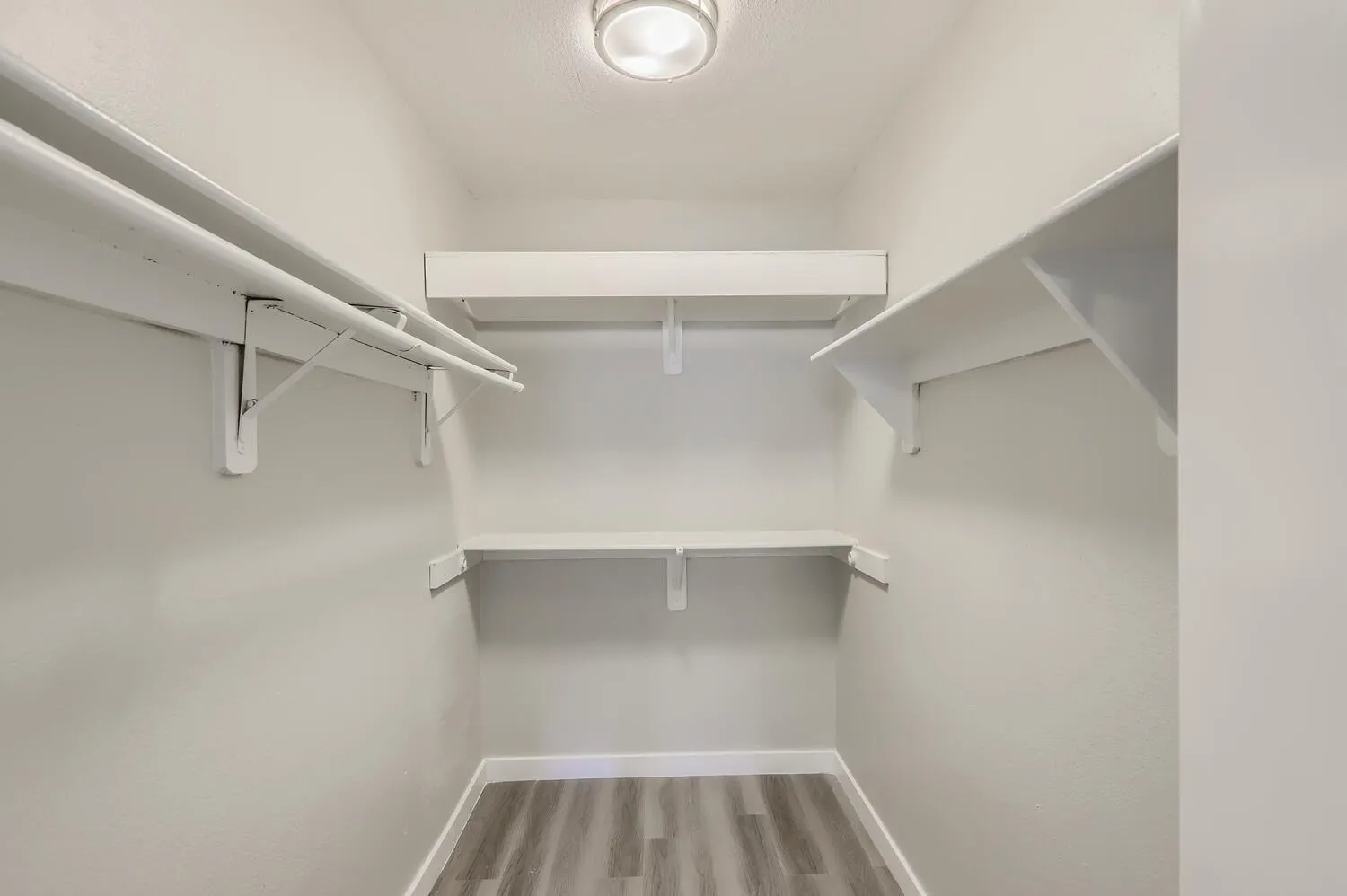 Walk-in closet, white shelving, hanging rods, wood-style plank flooring, ceiling light