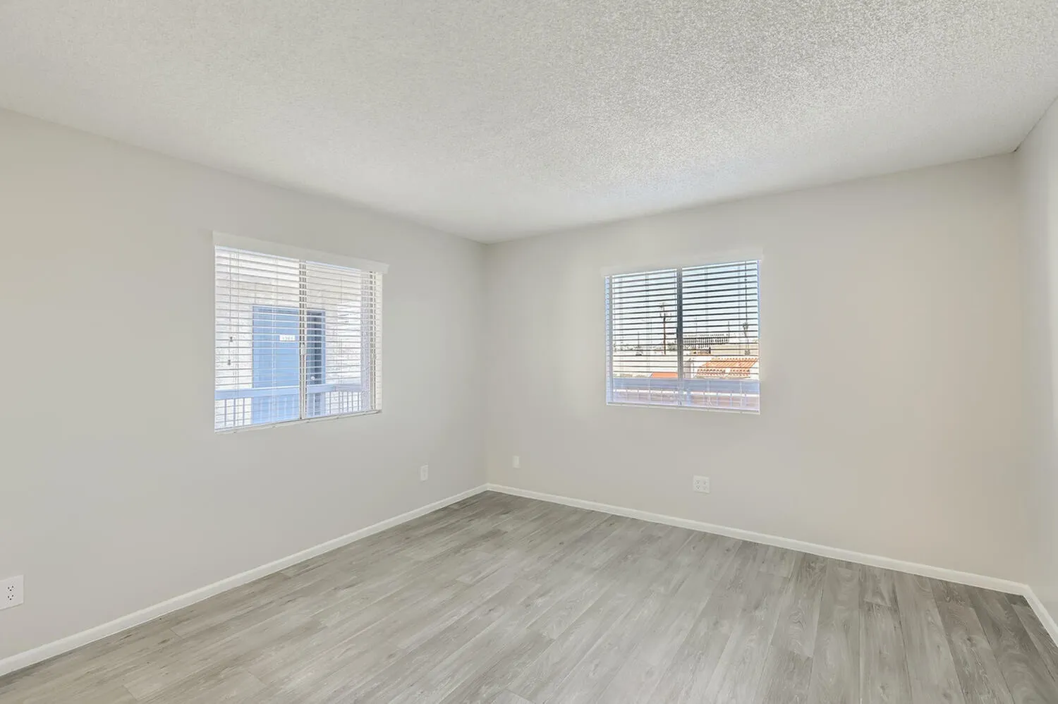 Bedroom, wood-style plank flooring, two windows with shutters, white walls, textured ceiling