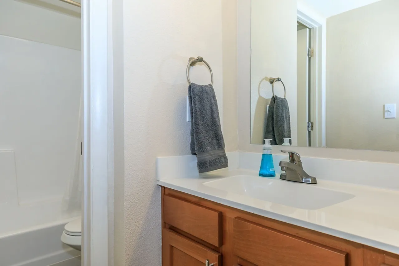 Bathroom, white quartz countertop, wood cabinetry, large mirror, towel bars