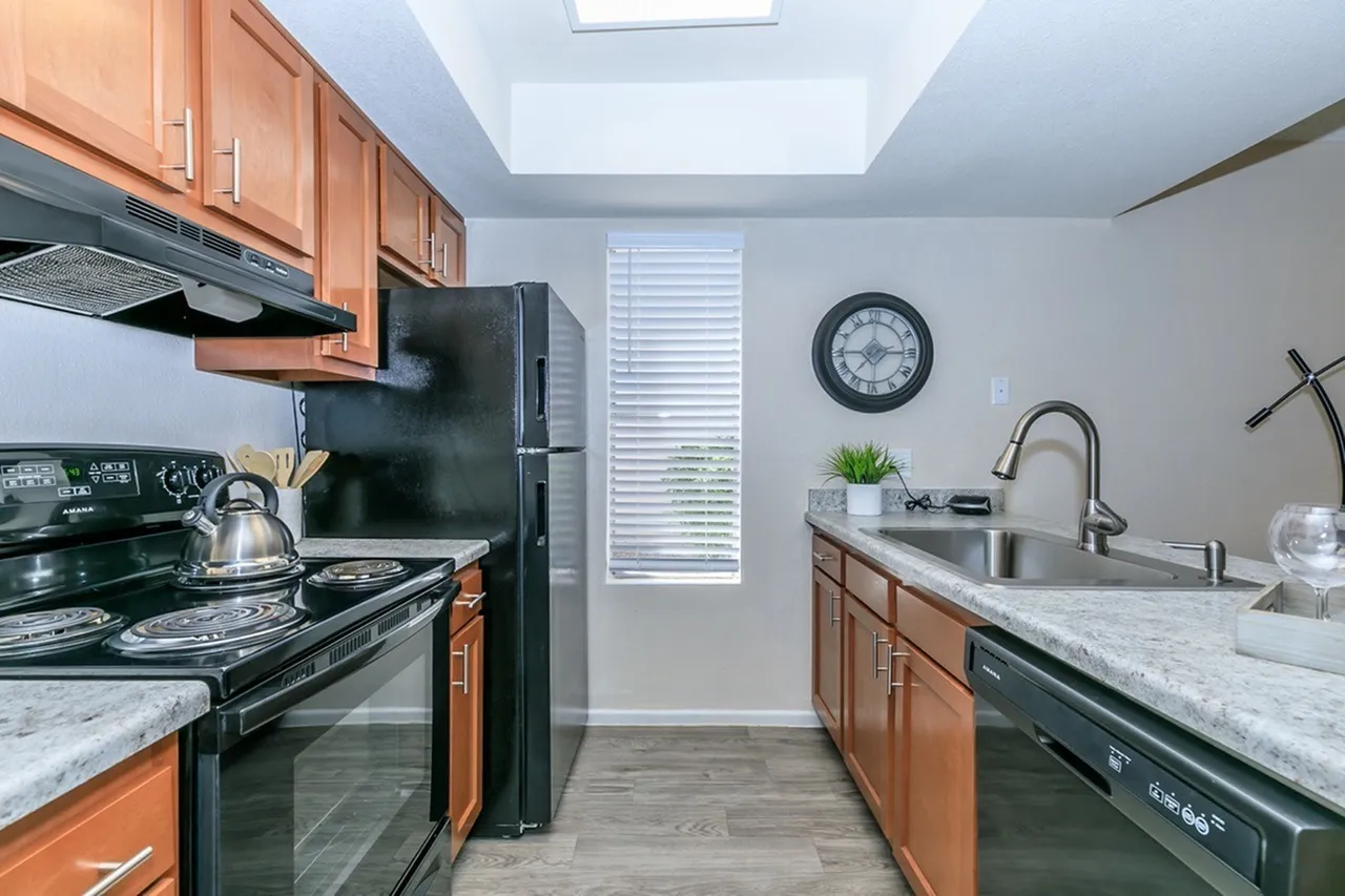 Kitchen, wood cabinetry, quartz countertops, black stove and refrigerator, wood-style plank flooring