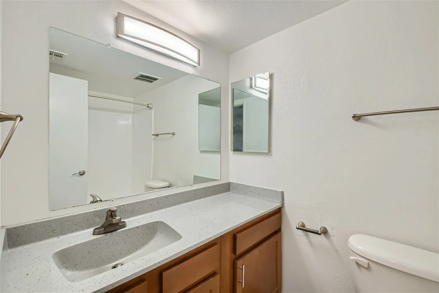 Primary bathroom, white quartz countertops, wood vanity cabinetry, large mirror, brushed nickel fixtures