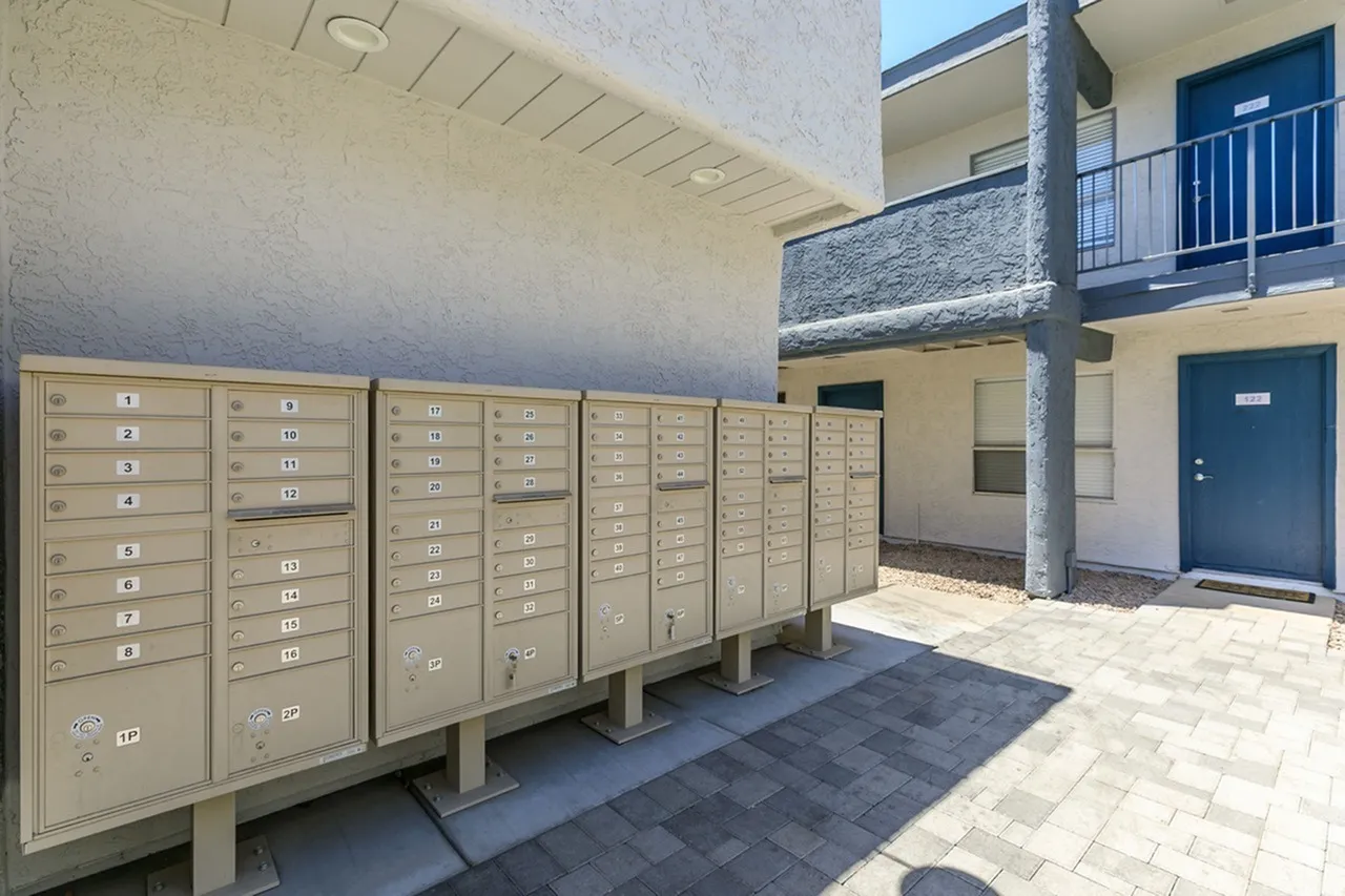 Multiple beige mailboxes in rows, concrete column, paved courtyard, apartment building