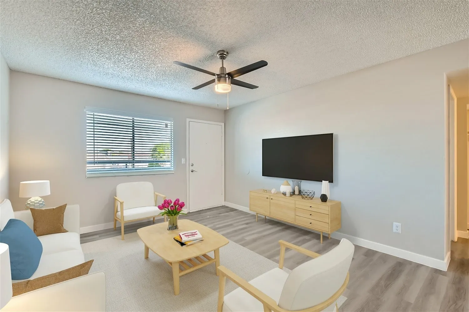 Living room, wood-style plank flooring, ceiling fan, flat-screen TV, natural light from window