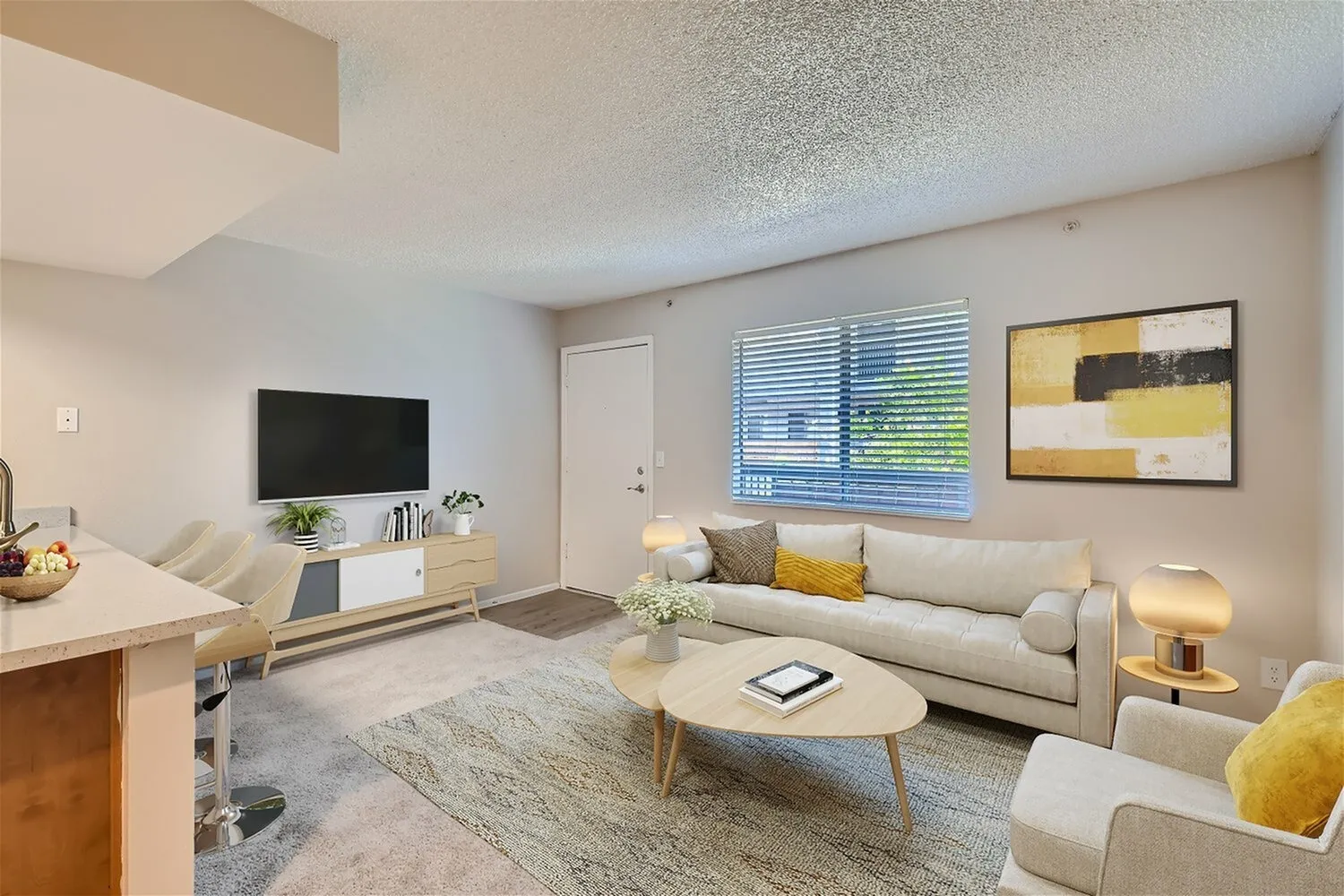 Living room with beige sofa, wood-style plank flooring, flat screen TV, abstract wall art, yellow accent pillow