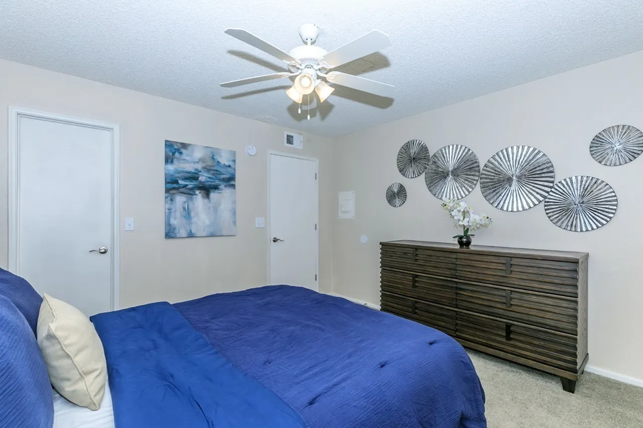 Bedroom, blue comforter, white pillows, ceiling fan, wall art, wood dresser