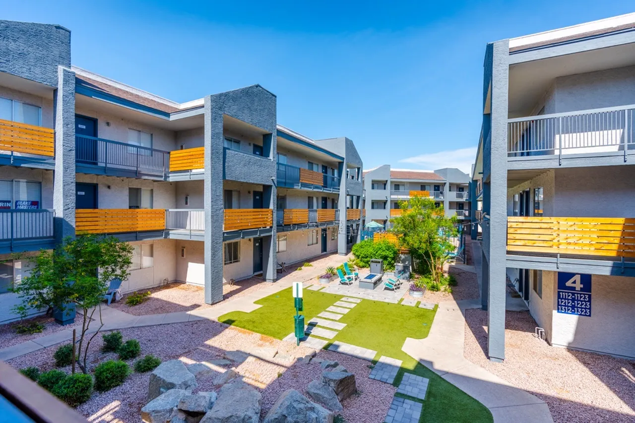 Courtyard with lawn, stone pathways, modern apartment buildings with yellow accent balconies