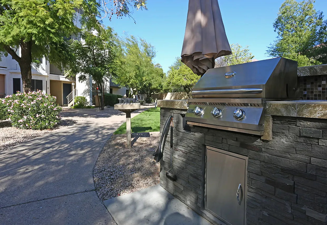 Patio with stainless steel built-in grill, umbrella, stone accents, residential pathway