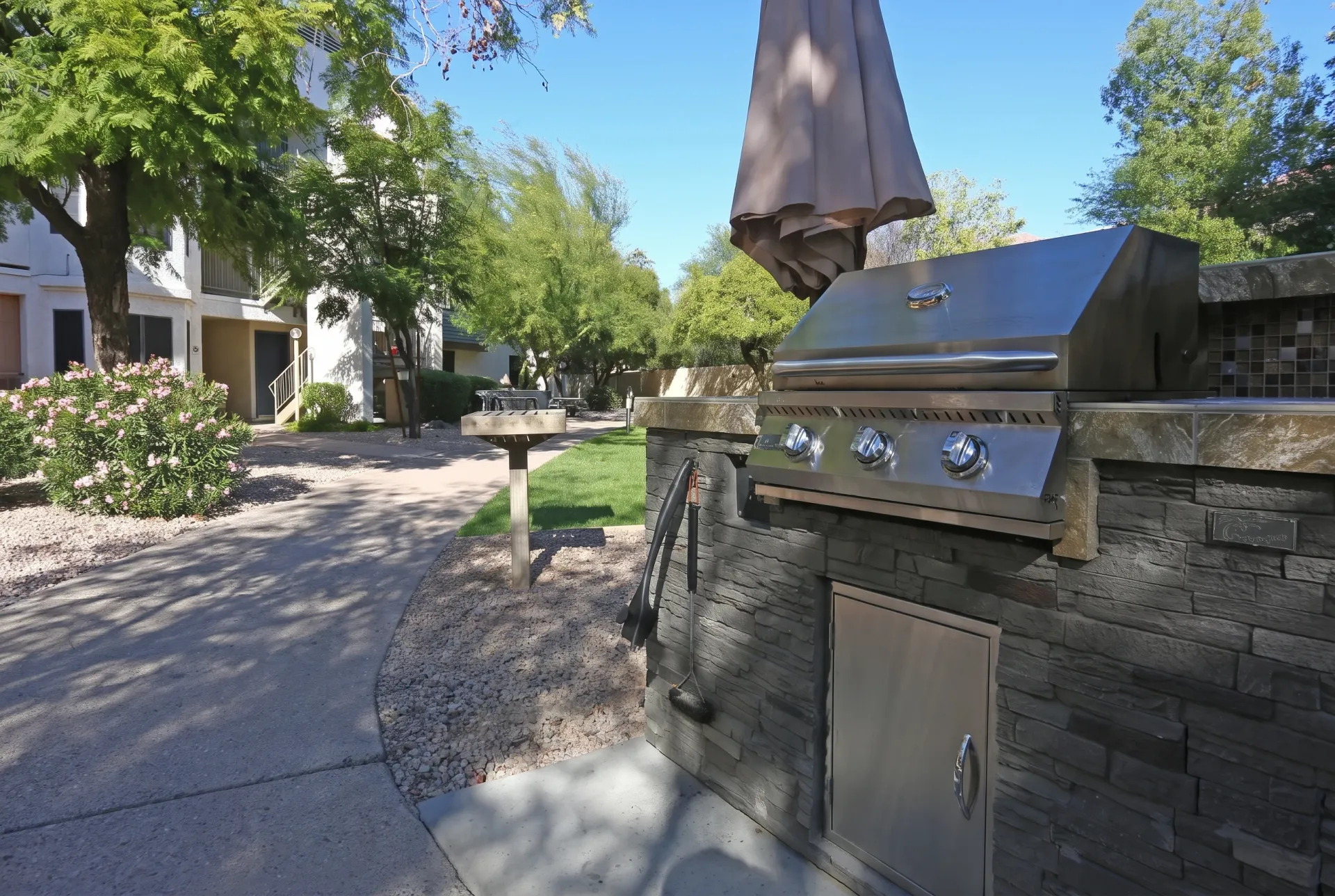 Patio with stainless steel built-in grill, umbrella, stone accents, residential pathway