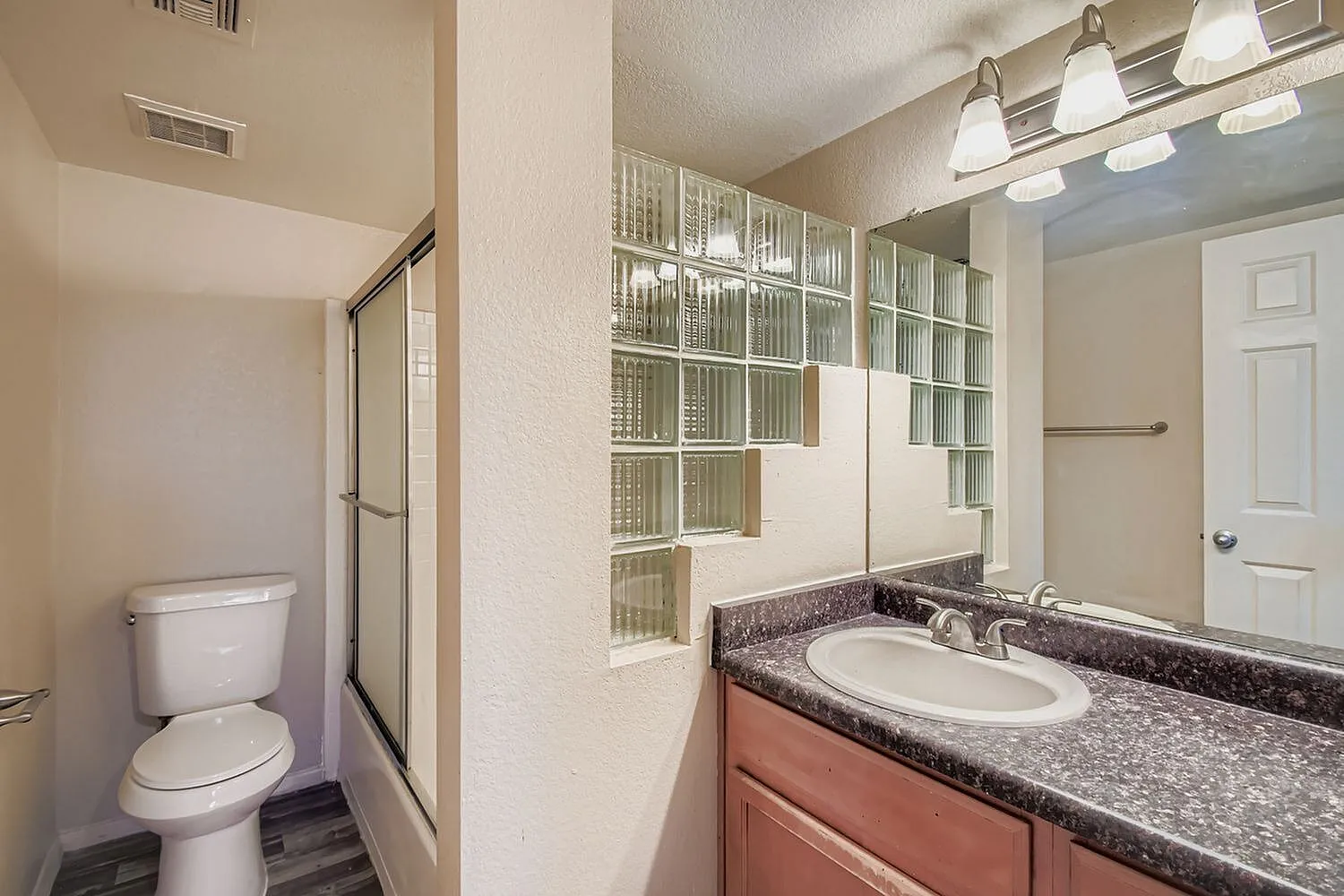 Primary bathroom, dark granite countertop, single sink vanity, glass-front cabinetry, pendant lighting, wood-style plank flooring