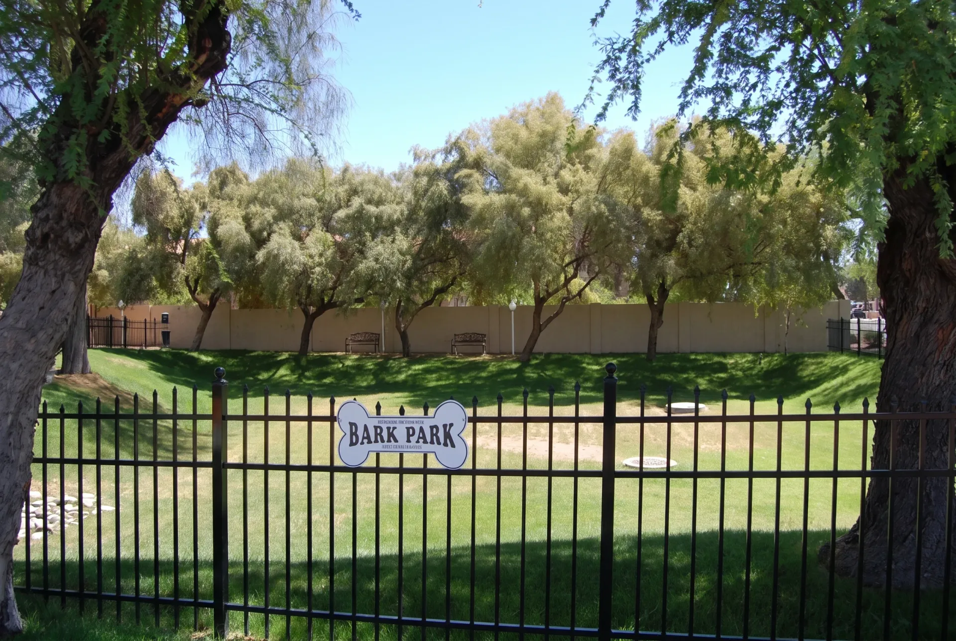 Bark park, black metal fence, manicured grass, mature trees, adobe walls
