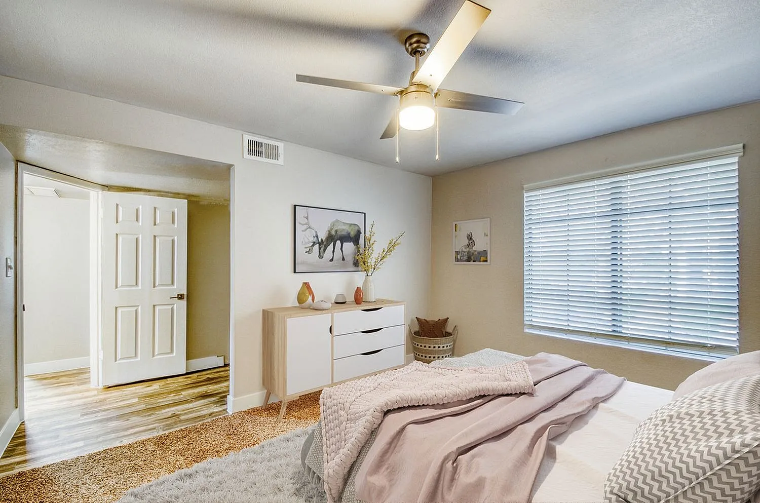 Primary bedroom, wood-style plank flooring, ceiling fan with light, dresser with décor, window with blinds