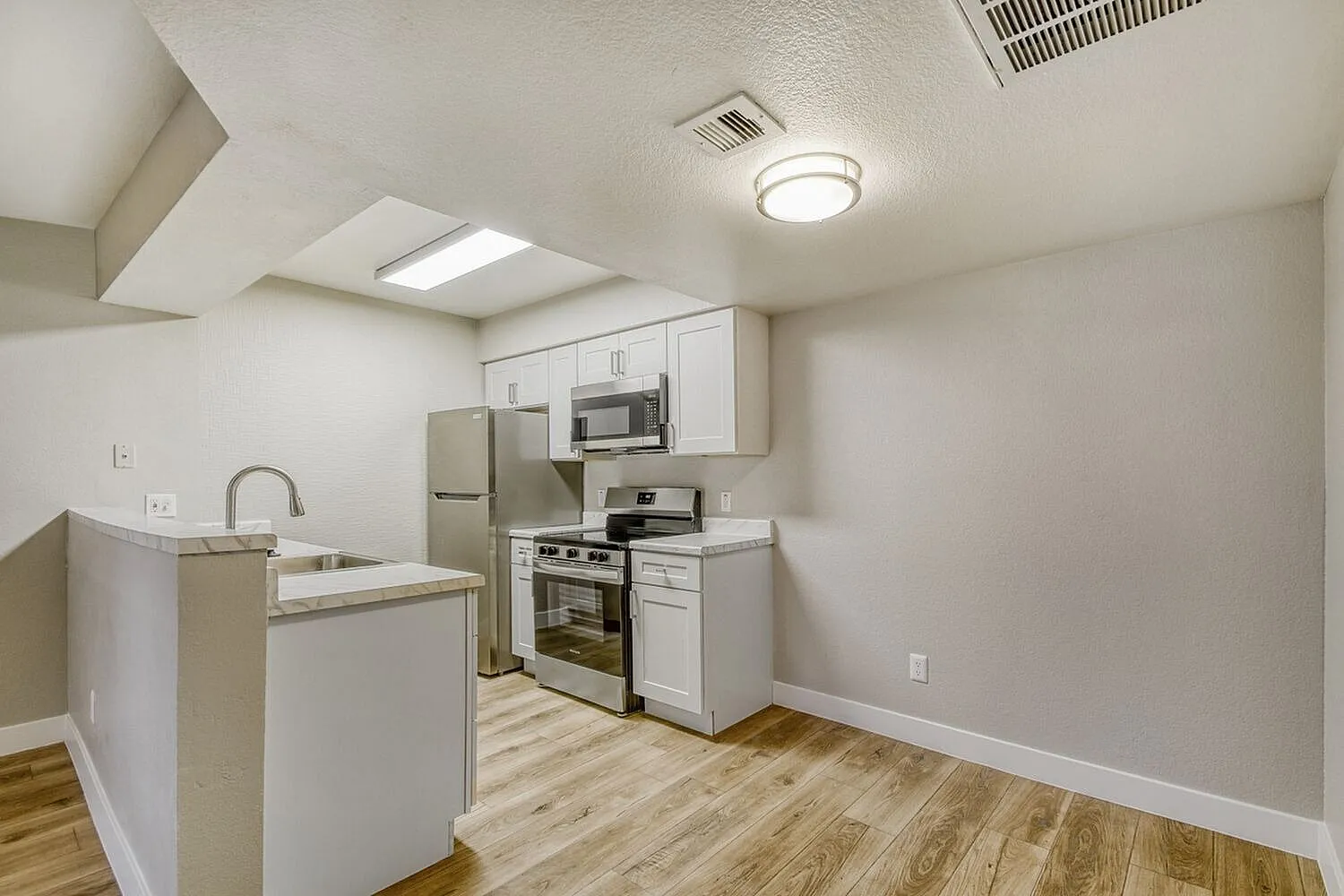 Kitchen, white shaker cabinetry, stainless appliances, wood-style plank flooring, island with sink