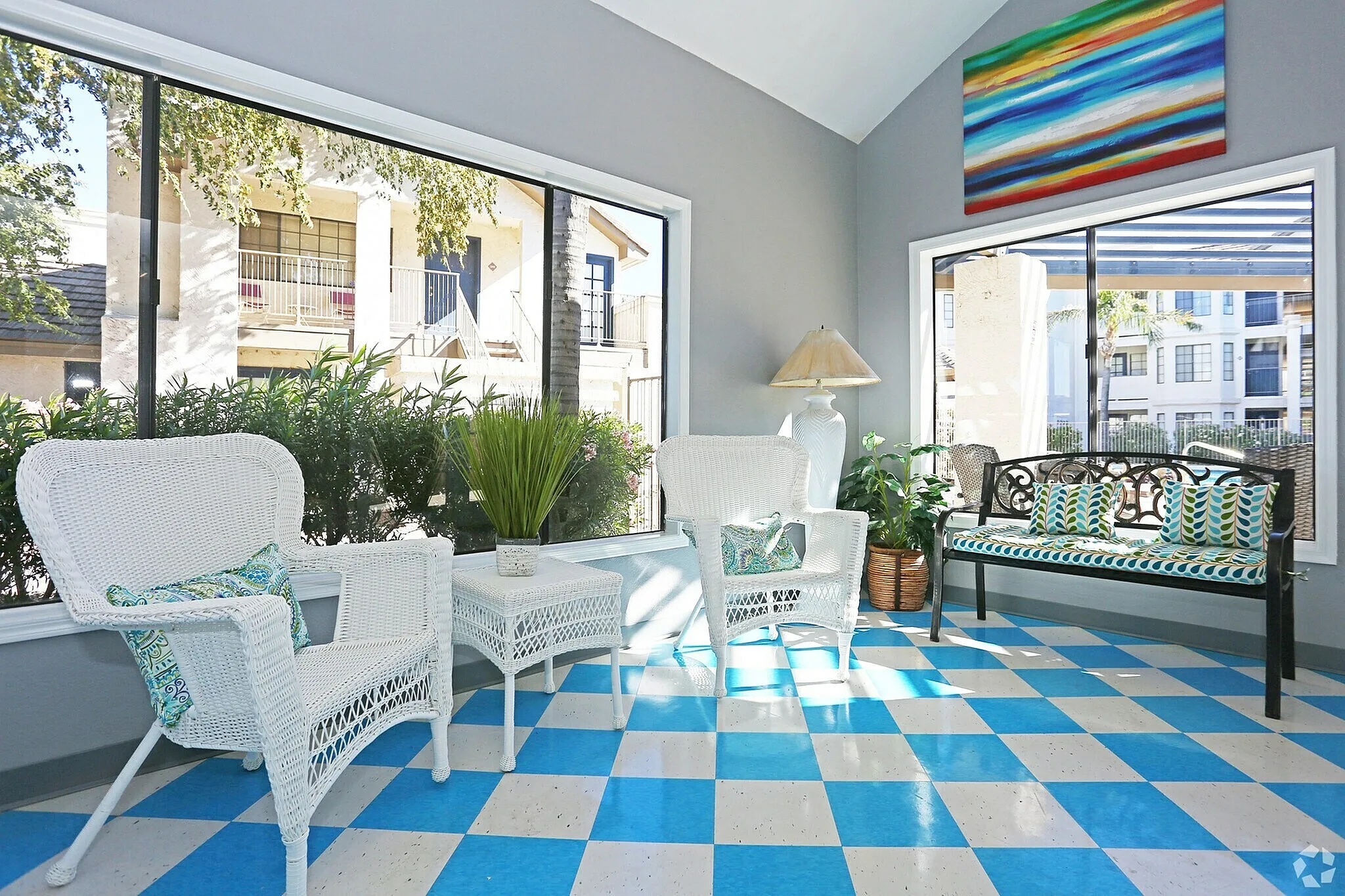 Sunroom, blue and white geometric floor, wicker furniture, glass doors and windows, potted plants
