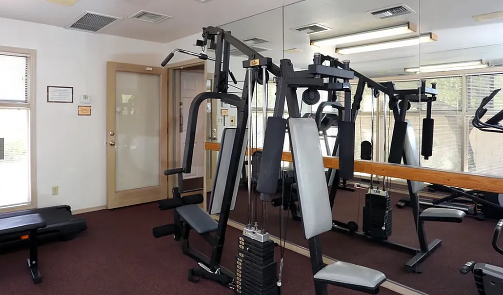 Fitness center, weight machines, burgundy plank flooring, ceiling lights, mirrors