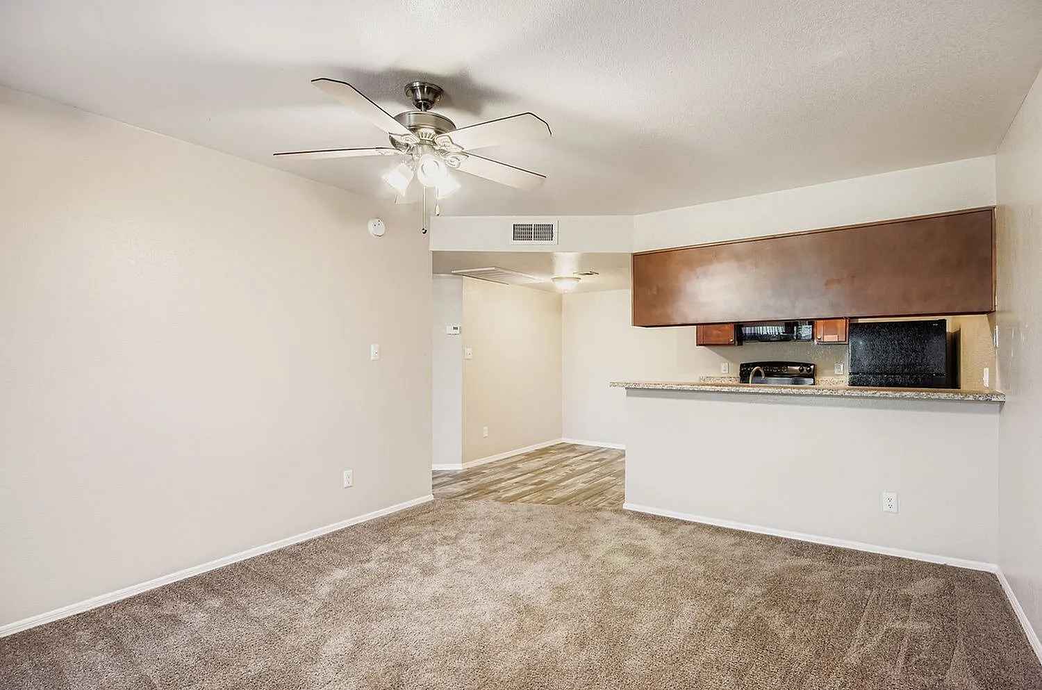 Living room with wood-style plank flooring, ceiling fan, brown cabinetry, kitchen counter, stainless appliances