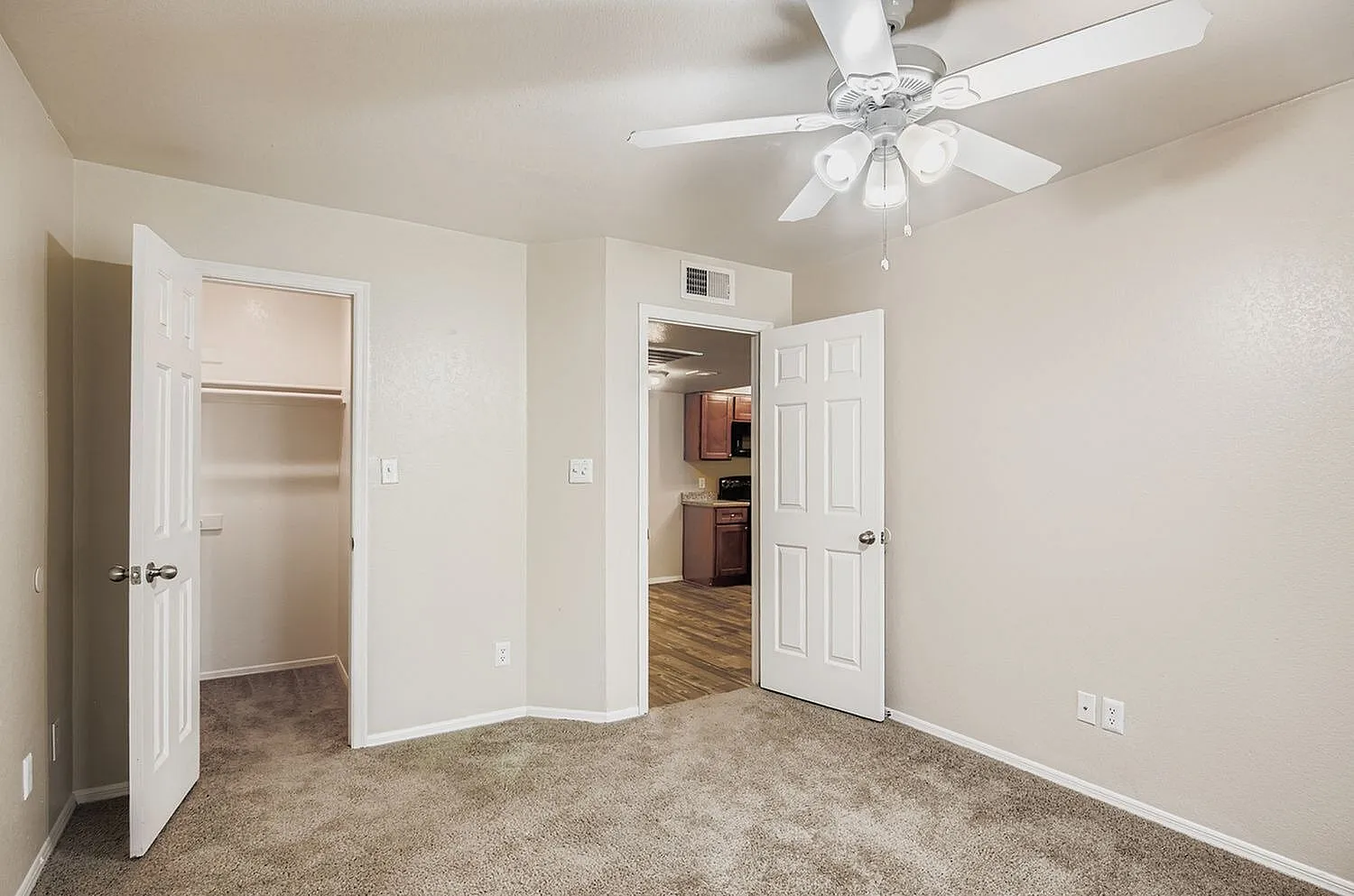 Bedroom, carpeted flooring, ceiling fan, white six-panel doors, neutral walls