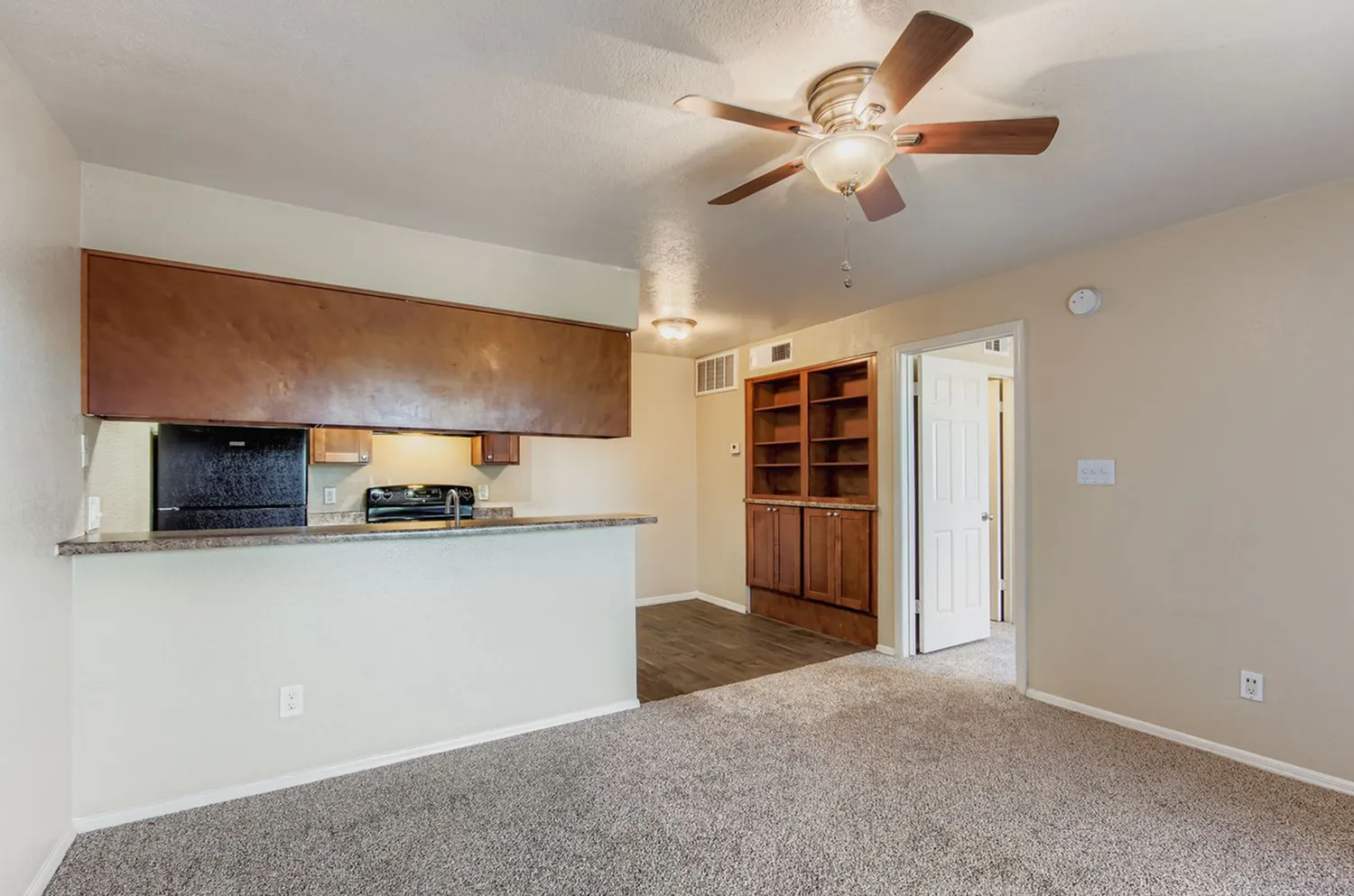 Open living space with wood-style plank flooring, ceiling fan, galley kitchen with wood cabinetry