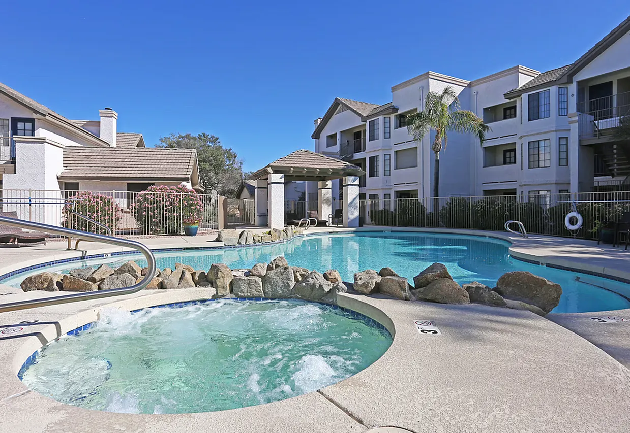 Resort pool area, spa tub, lounge seating, residential buildings, landscaping, clear blue sky