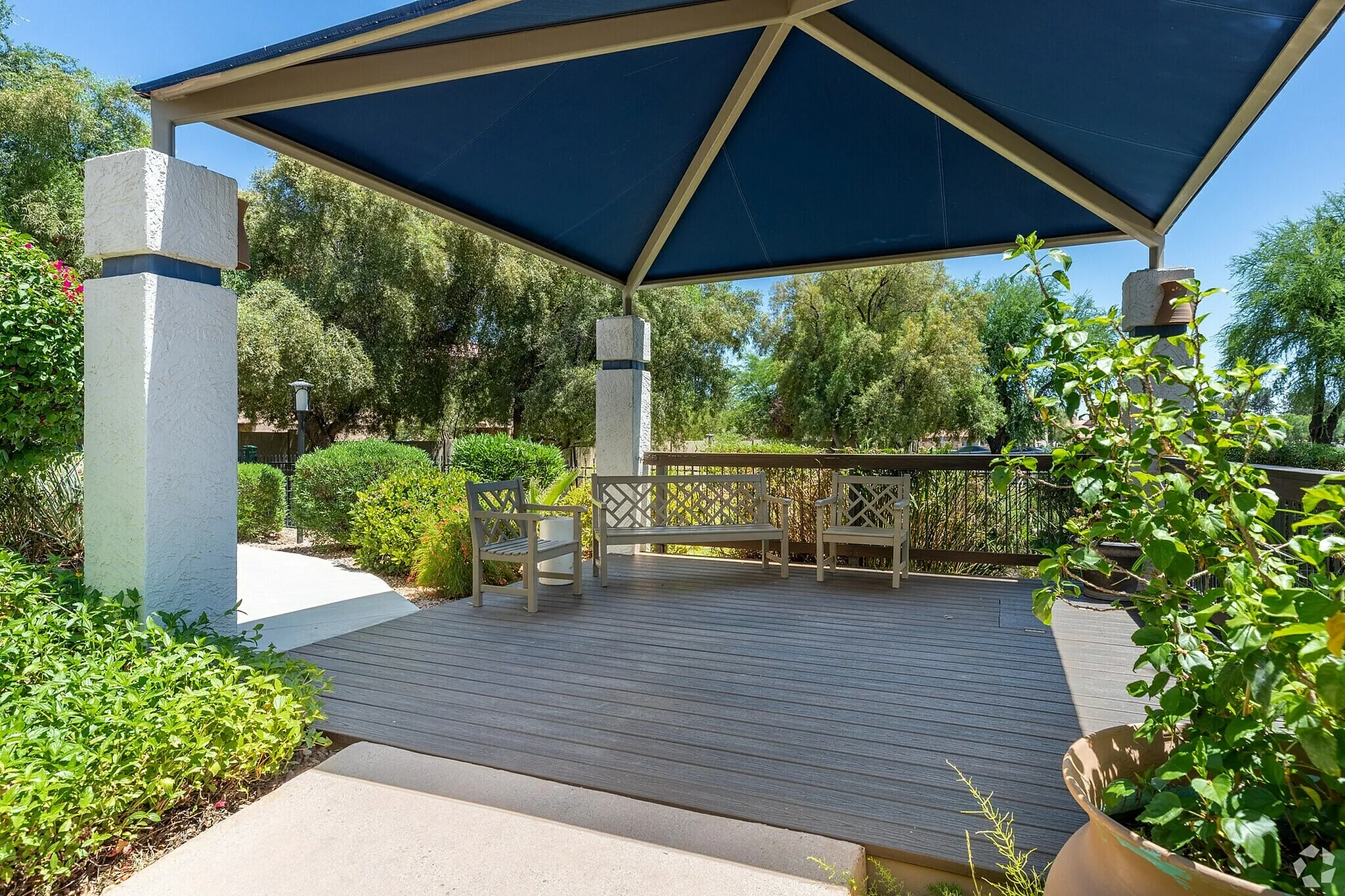 Covered patio, gray composite decking, blue shade structure, wood bench seating, landscaping
