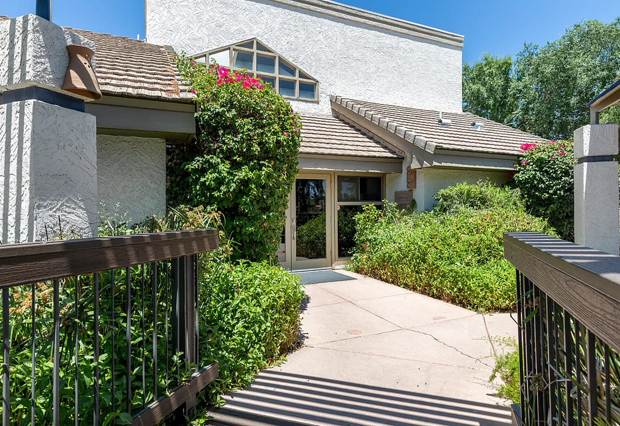 Courtyard entry with concrete pathway, dark metal railings, mature climbing vines, pink flowering plants