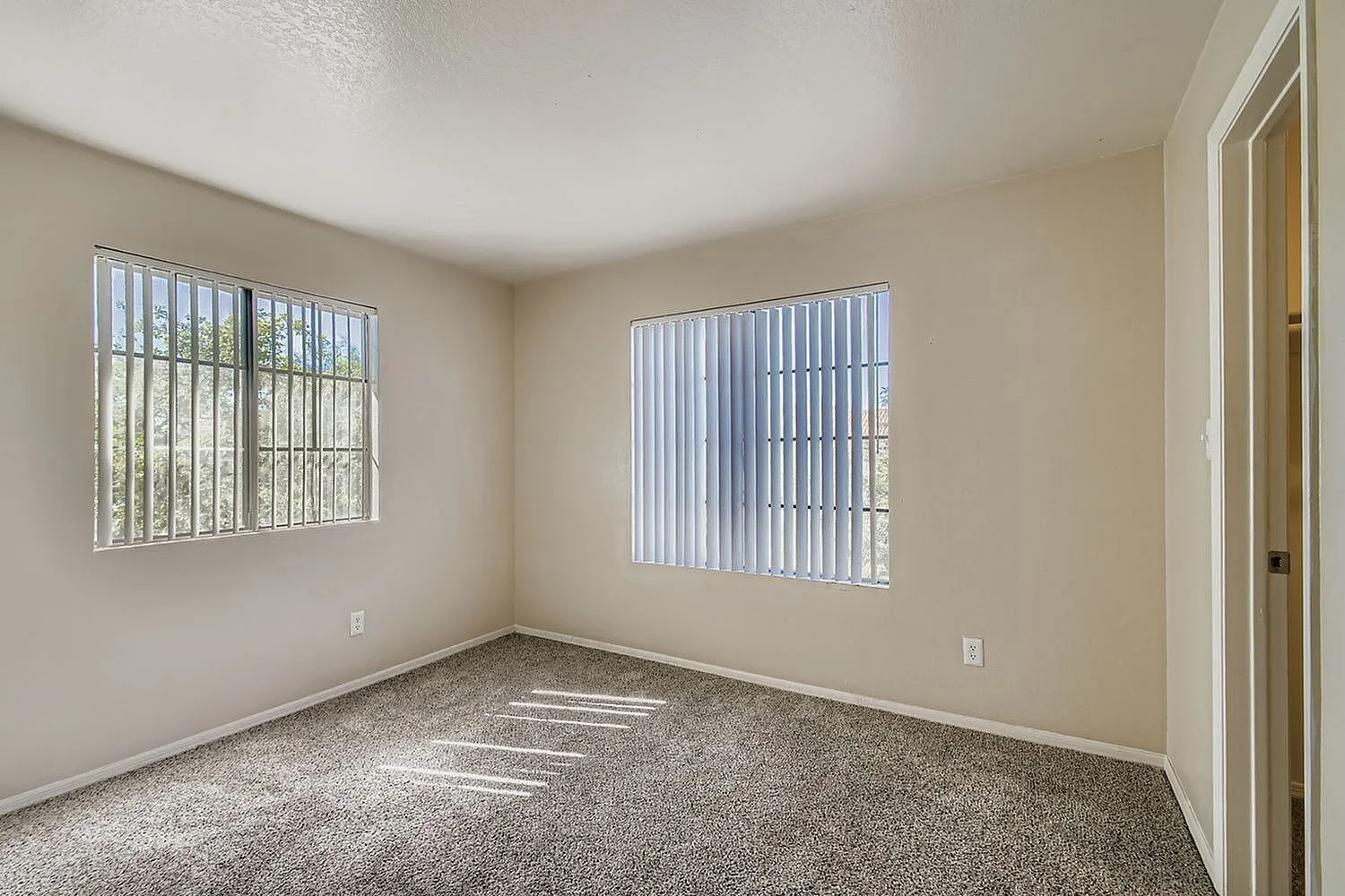 Bedroom, beige walls, carpeted flooring, two barred windows, white trim