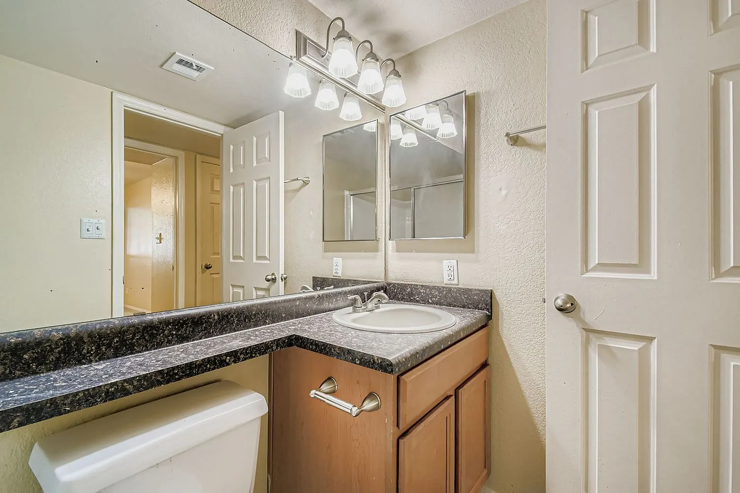 Bathroom, dark granite countertop, wood cabinetry, round sink, vanity mirror with light fixture