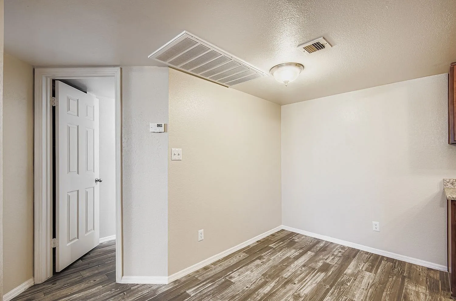 Bedroom, wood-style plank flooring, white six-panel door, ceiling vent and light fixture